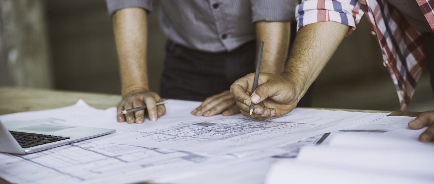 Close up of two architect's hands holding pencils over some building blueprints.